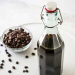 DIY Coffee Liqueur in a swing top bottle next to a small bowl of coffee beans.