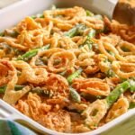 Closeup photo of a green baking dish of green bean casserole topped with fried onions along with a serving spoon